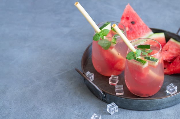 Summer watermelon drink in two glasses with eco straws and sliced fruit on a metal tray