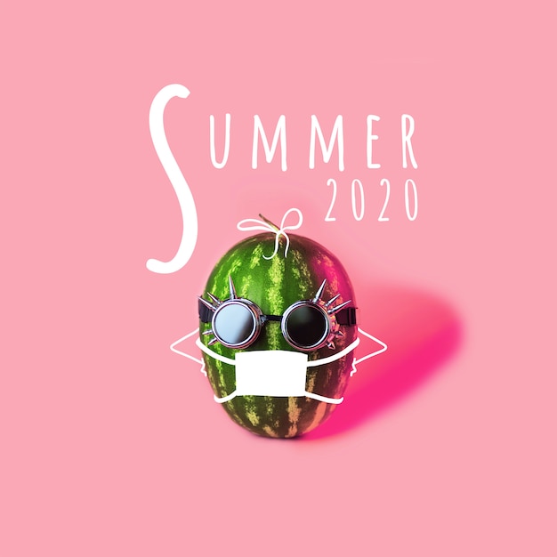 防護マスクとピンクの背景のメガネで夏のスイカ。保護をテーマとしたコンセプト。