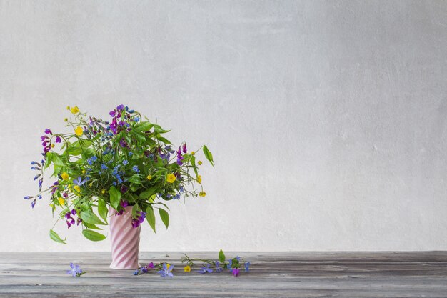 Summer wild flowers in pink ceramic vase on white background