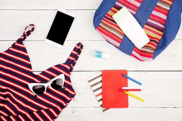 Летняя женская мода с красочной полосатой сумкой, купальником, смартфоном, солнцезащитными очками и блокнотами