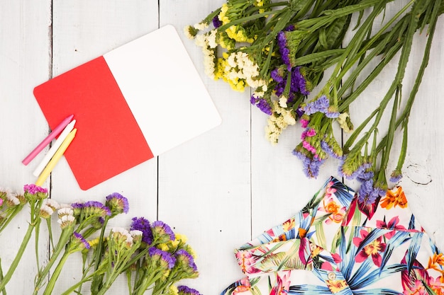 Foto le donne di estate hanno messo con il blocco note di fiori variopinti del vestito e le matite su fondo di legno bianco