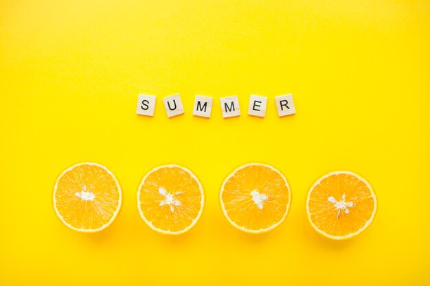 Photo summer word in white cubes with half oranges in a row isolated on yellow background