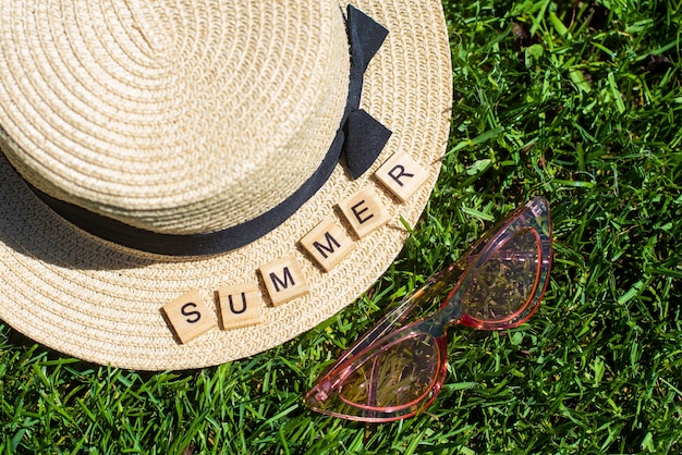 Photo summer written on wooden cubes over a straw hat and pink sunglasses on grass background