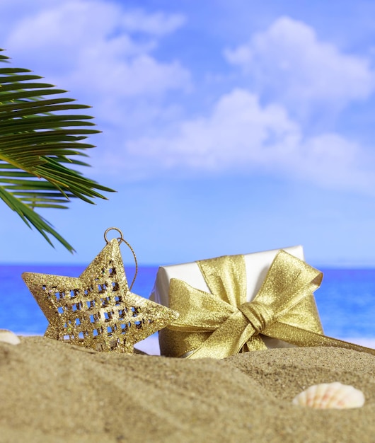 Summer xmas holidays concept Christmas ornament on sandy beach with palm tree blue sea and sky background