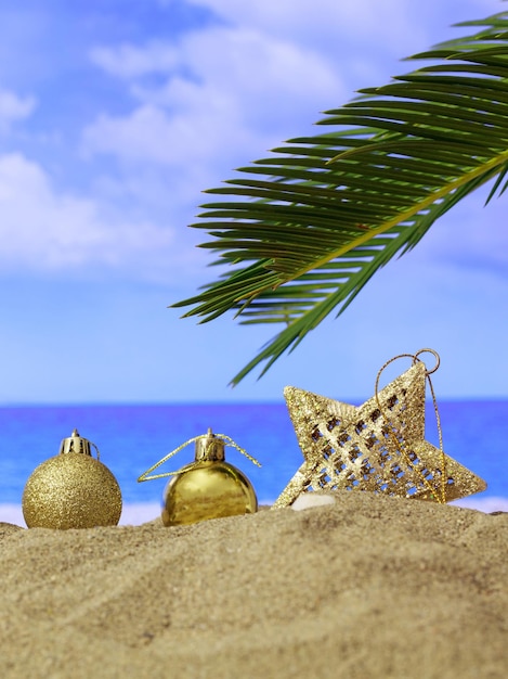 Summer xmas holidays concept Christmas ornaments on sandy beach with palm tree blue sea and sky background