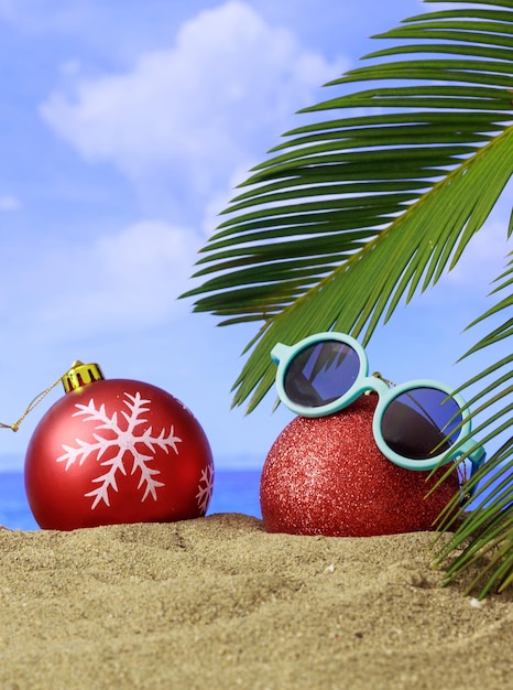 Summer xmas holidays concept Christmas ornaments on sandy beach with palm tree blue sea and sky background