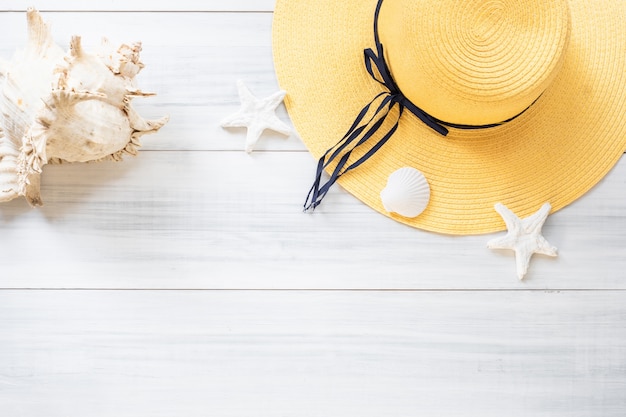 of summer yellow female hat with sunglasses and shell decoration on wood table.