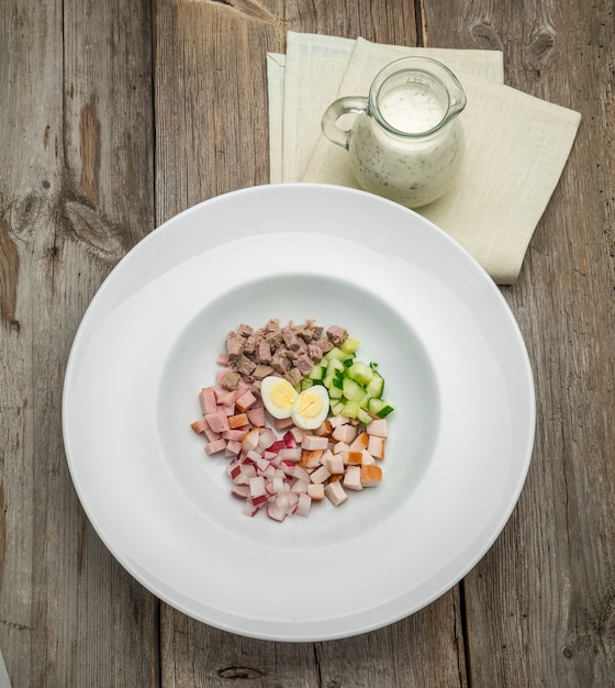 Summer yoghurt cold soup with radish, cucumber, and dill on wooden table. Russian Okroshka.