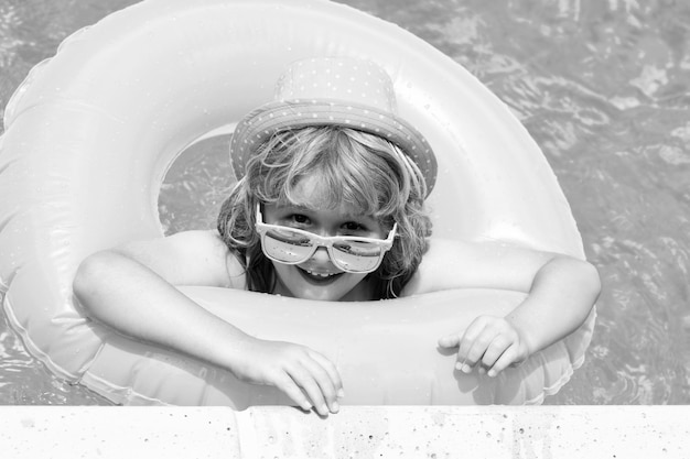 Летнее веселье Ребенок плавает в бассейне, играет с плавающим кольцом Улыбающийся милый ребенок в солнечных очках плавает с надувными кольцами в бассейне в летний день