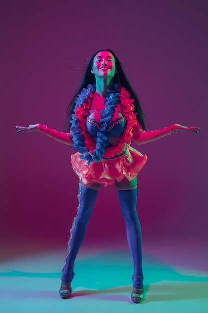 Summertime. Hawaiian brunette model on purple  wall in neon light. Beautiful women in traditional clothes smiling, dancing and having fun. Bright holiday's, celebration colors, festival.