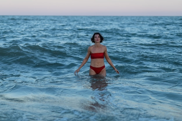 Concetto di ricreazione estiva. bella giovane donna sexy con un corpo sottile addestrato in forma indossando bikini rosso costumi da bagno posa su una spiaggia sabbiosa. modello femminile di moda vicino al mare.