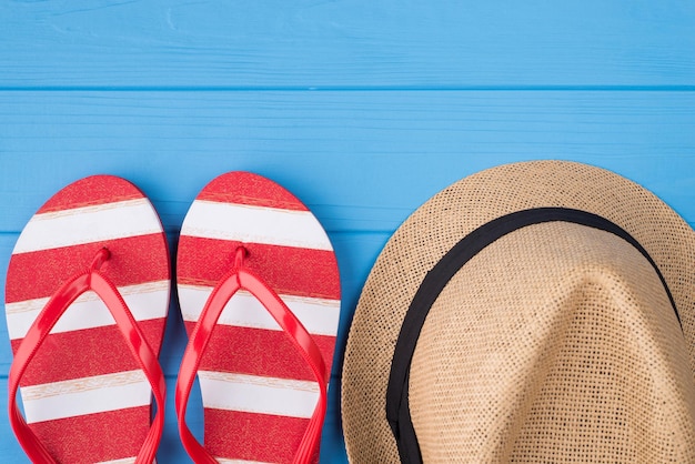 Summertime relax concept. Top above overhead view photo of striped flipflops and hat isolated on blue wooden background