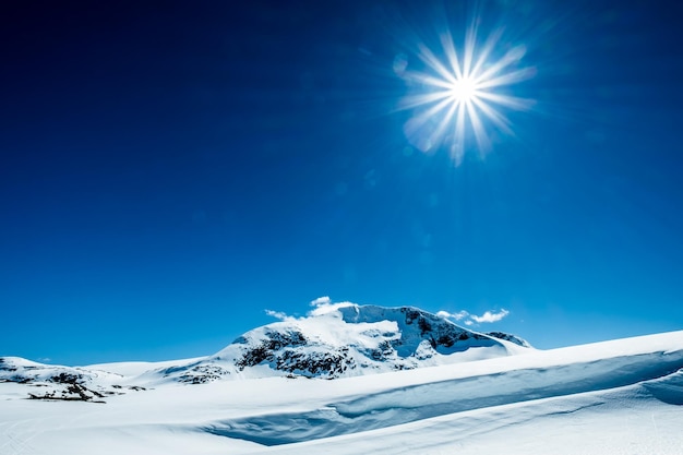 Sun in a blue sky over snowy mountain.