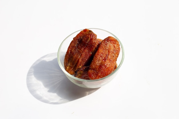 Sun dried bananas in glass bowl on white surface.