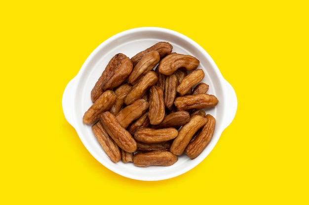 Sun-dried bananas in whitec plae on yellow background.