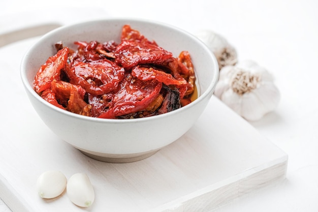 Sun dried tomatoes  on white bowl white wooden background Dried tomatoes with olive oil salt her