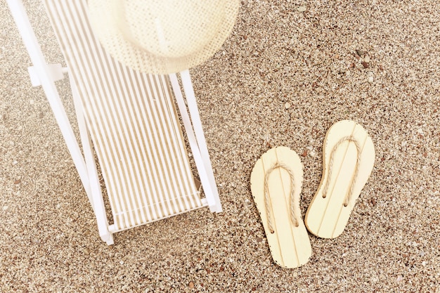 Sun hat on sunbed and pair of flip-flops on sandy beach under bright sun. Copy space. Summer holidays.