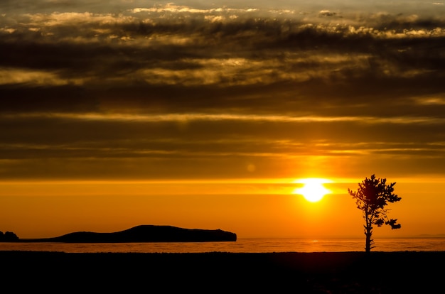 Sole sopra il lago, montagna e albero al tramonto nella luce di contrasto con le nuvole