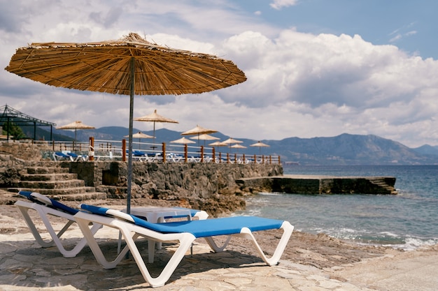 Sun loungers stand under a beach umbrella near water