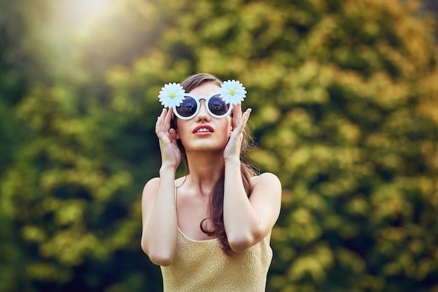 The sun loves her Portrait of an attractive young woman wearing sunglasses while holding them and standing outside in nature during the day