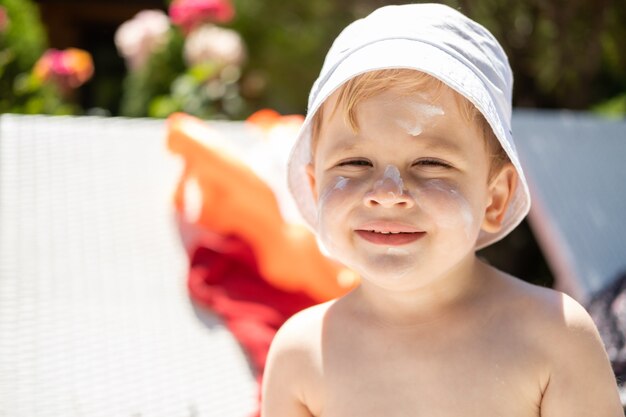 Sun protection close up portrait of boy face with sunscreen suntan lotion before tanning during a su...