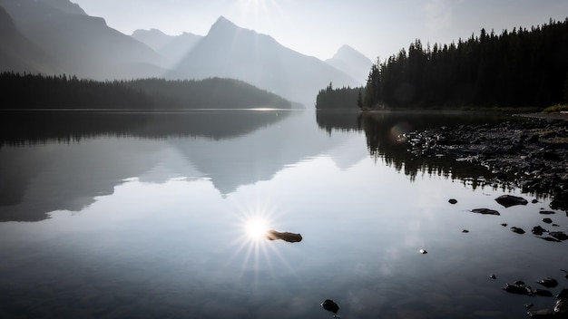 Sun reflecting in still alpine lake surrounded by mountains and forest Jasper NP Canada