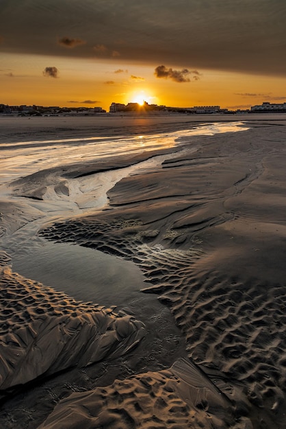 The sun rises behind the church and the buildings of the coast behind the puddles of the beach