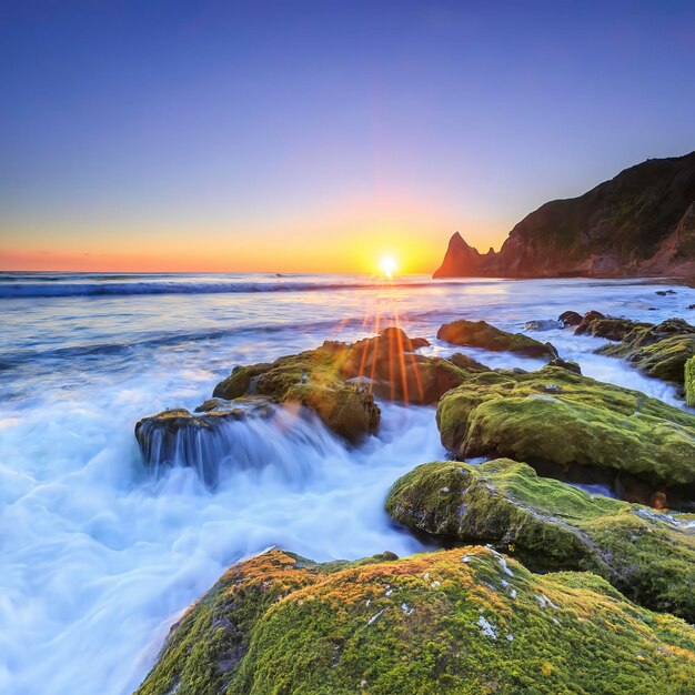 The sun rises over a gorgeous beach with mossy rocks