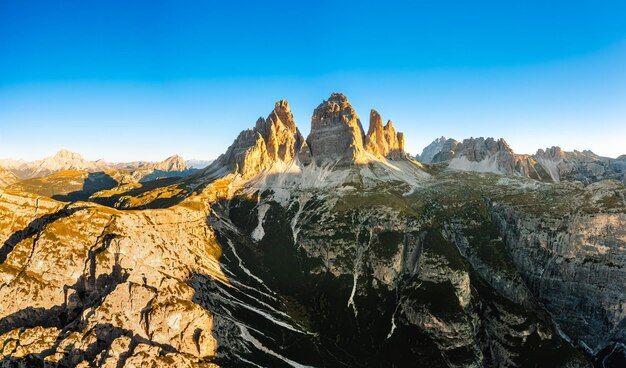 Foto il sole sorge sulle maestose cime delle tre cime di lavaredo alte cime rocciose sotto un cielo limpido a