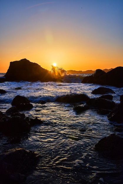 Sun sets on beach with waves and rocks