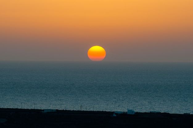 The sun sets behind the horizon line on the sea.