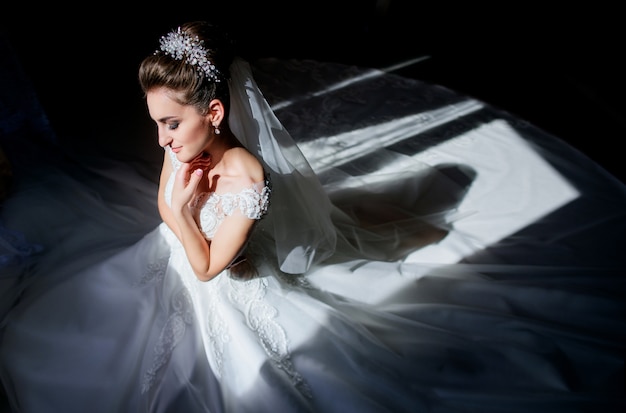 Sun and shadows play on the face of gorgeous bride sitting in the dark room