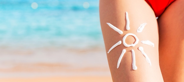 Sun shape is made of sunscreen on woman's leg at the sea