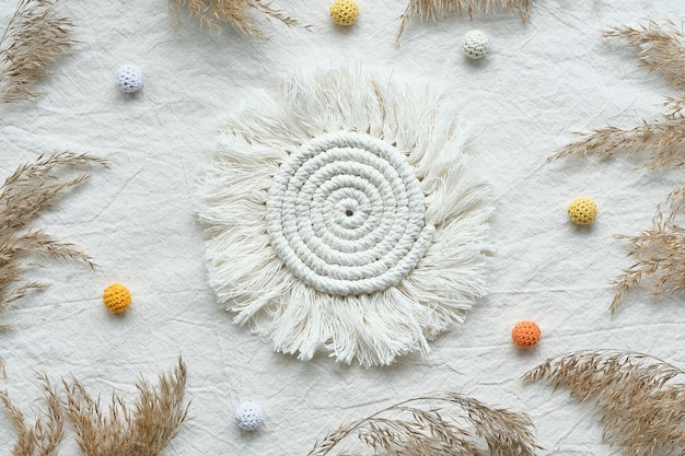 Sun shaped macrame pad Textile flat lay with dry reeds pampas grass and knitted cotton balls Off white tablecloth background flat lay