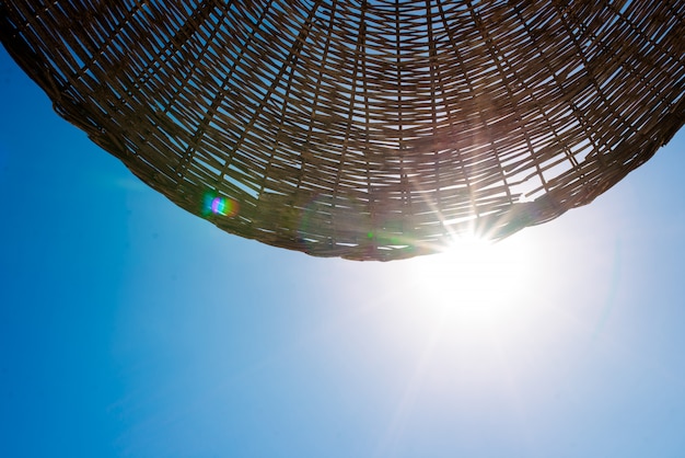 The sun shines through the umbrella on the beach.