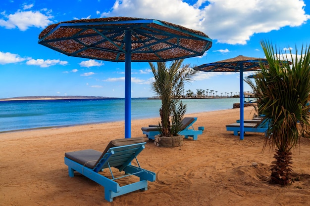 Sun umbrellas and chaise lounges on tropical beach. Concept of rest, relaxation, holidays, resort