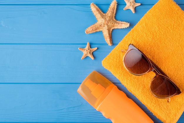 Sunbathing and relaxing concept. Top above overhead view close-up photo of sunscreen sunglasses yellow towel and starfish isolated on blue wooden background with copyspace