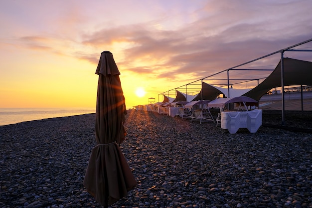 カラフルなオレンジ色の夕日、ビーチの波、幾何学傘、無人の沈黙の海岸に沈む夕日のビーチのサンベッド。