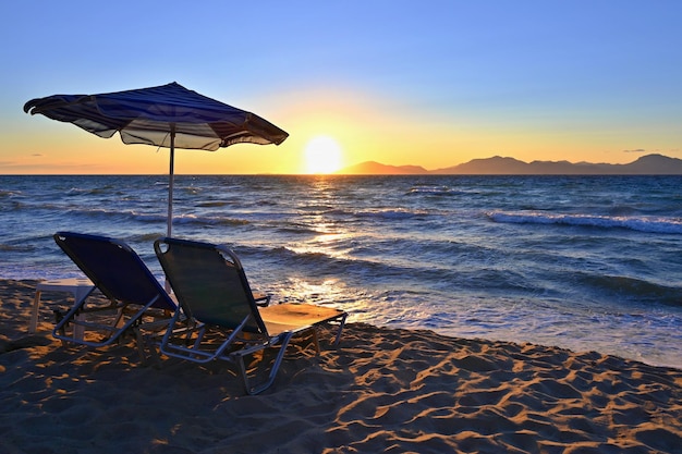 海に沈む夕日のビーチのサンベッドと傘休暇夏休みや旅行のための美しいコンセプト