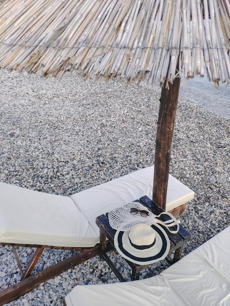 Sunbeds with straw umbrella on the pebble beach Hat bag and glasses equipment