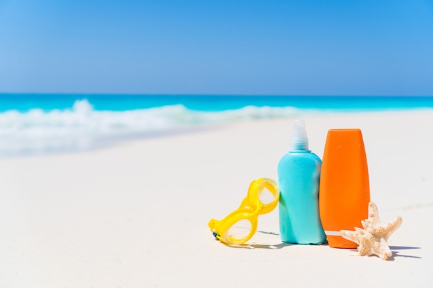 Suncream bottles, goggles, starfish on white sand beach with ocean views