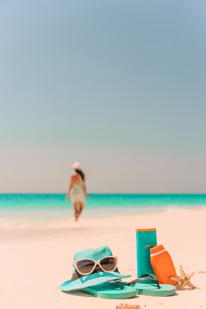 Suncream bottles, sunglasses, flip flop on white sand background ocean