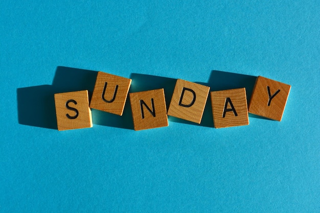 Sunday word in wooden alphabet letters isolated on bright blue background