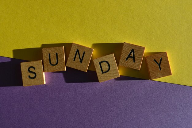 Sunday word in wooden alphabet letters isolated on bright yellow and purple background