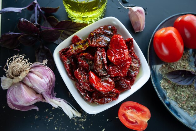 Sundried tomatoes in a bowl surrounded by ingredients spices garlic and basil to prepare Rustic style top view