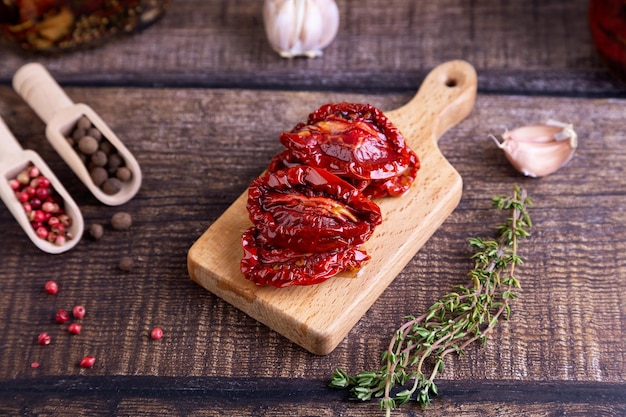 Sundried tomatoes in olive oil on a mini board with pepper garlic and thyme in a rustic style Selective focus closeup