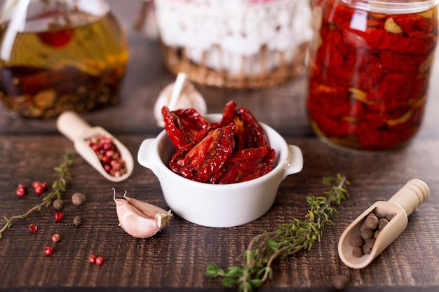 Sundried tomatoes in olive oil in a white bowl with pepper garlic and thyme in a rustic style Selective focus closeup