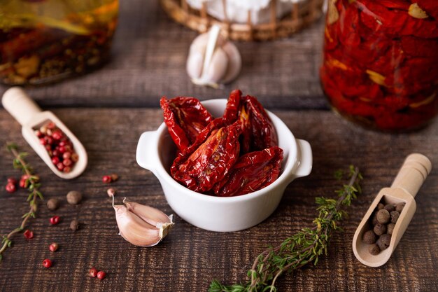 Sundried tomatoes in olive oil in a white bowl with pepper garlic and thyme in a rustic style Selective focus closeup