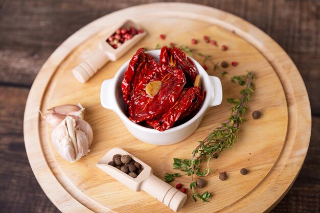 Sundried tomatoes in olive oil in a white bowl with pepper garlic and thyme on a wooden board Home cooking rustic style Selective focus closeup