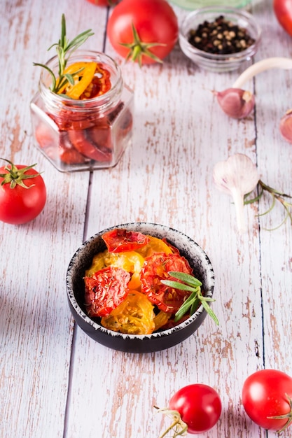 Sundried tomatoes with spices and herbs in a bowl and fresh vegetables on the table Vertical view